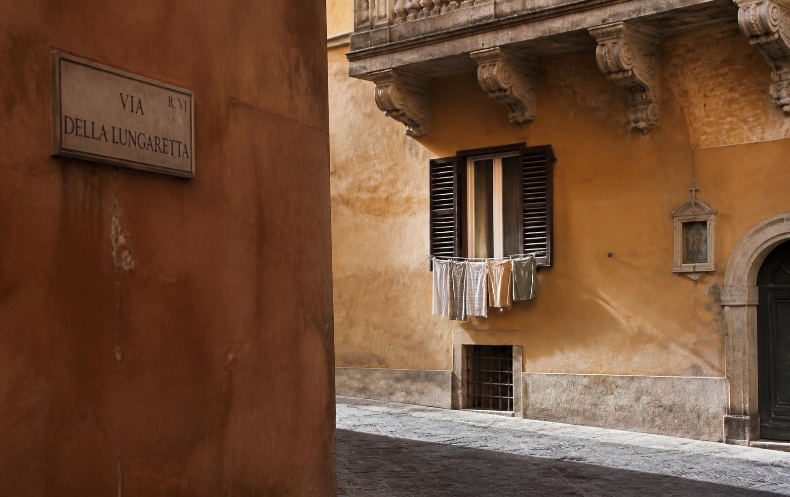 A narrow Italian street in early light, ochre stucco, shuttered window and stone paving